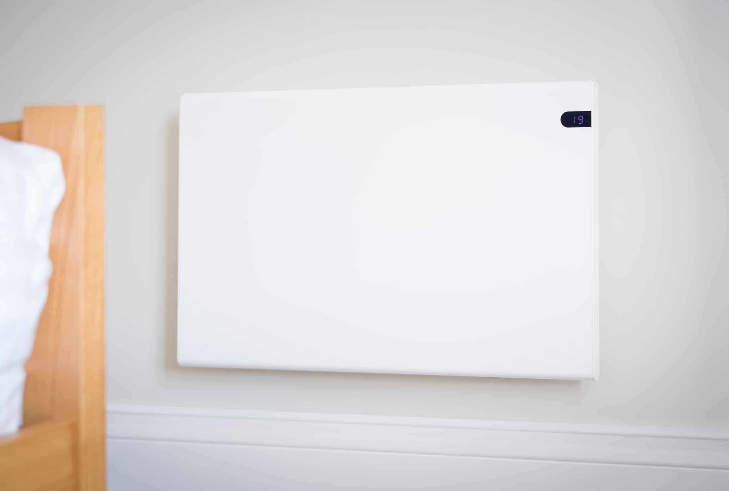 Chauffage mural électrique blanc moderne dans une chambre, affichant une température de 19 degrés, près d'un cadre de lit en bois clair.