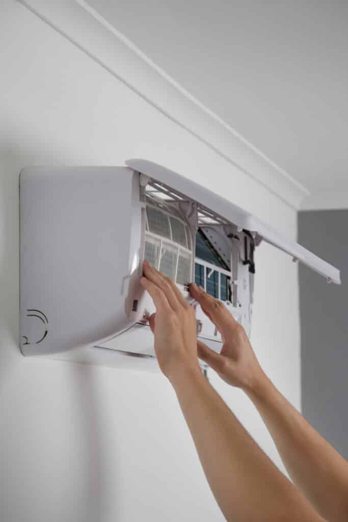 Nettoyage filtre climatiseur mural : entretien facile Mains nettoyant le filtre à air sale d'une unité intérieure de climatiseur mural blanc, entretien de la climatisation.