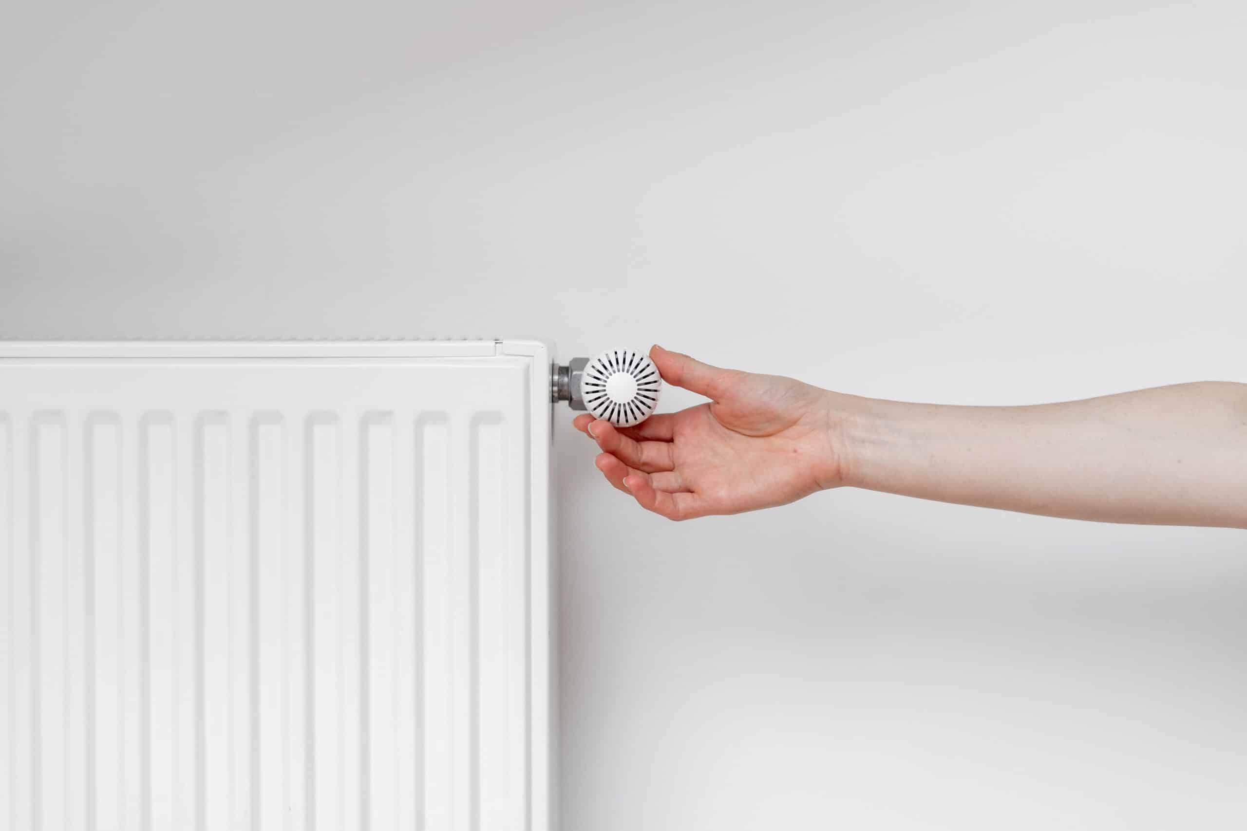 Main ajustant le thermostat blanc d'un radiateur moderne à panneaux contre un mur clair pour réguler le chauffage.