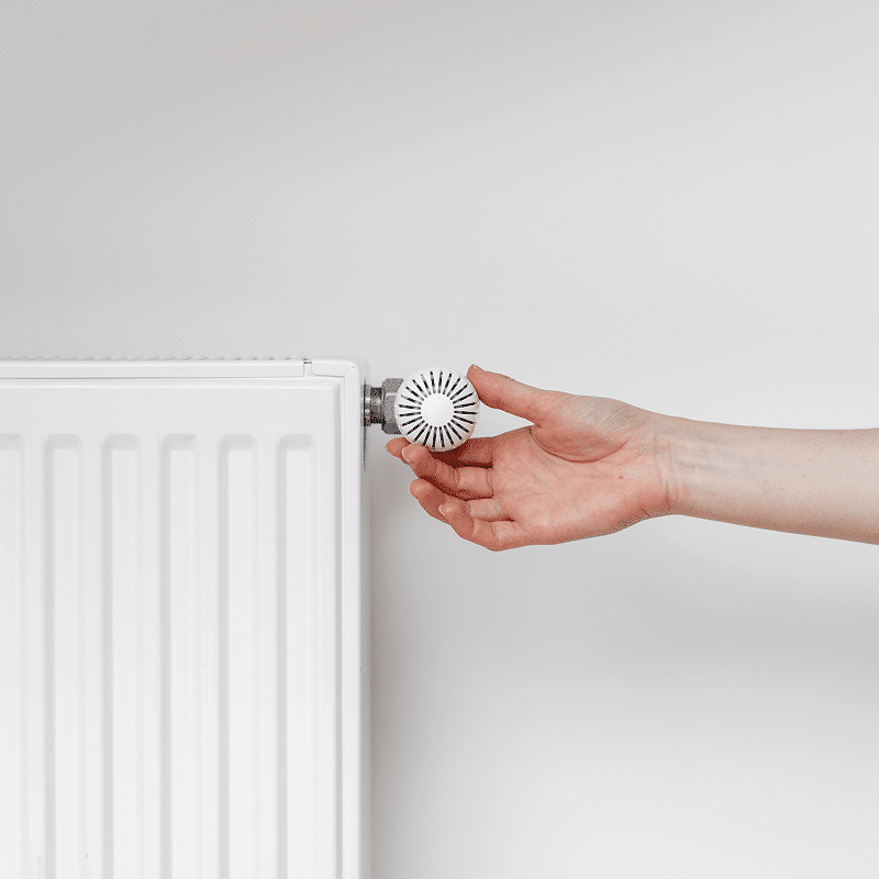 Une main ajuste la vanne thermostatique blanche d'un radiateur. Réglage de la température du chauffage pour économiser de l'énergie.